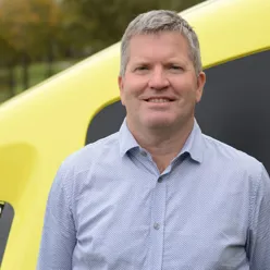A man standing in front of a yellow car